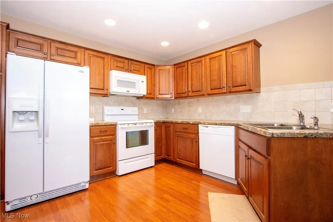 Kitchen featuring white appliances, a sink, brown cabinets, tasteful backsplash, and recessed lighting