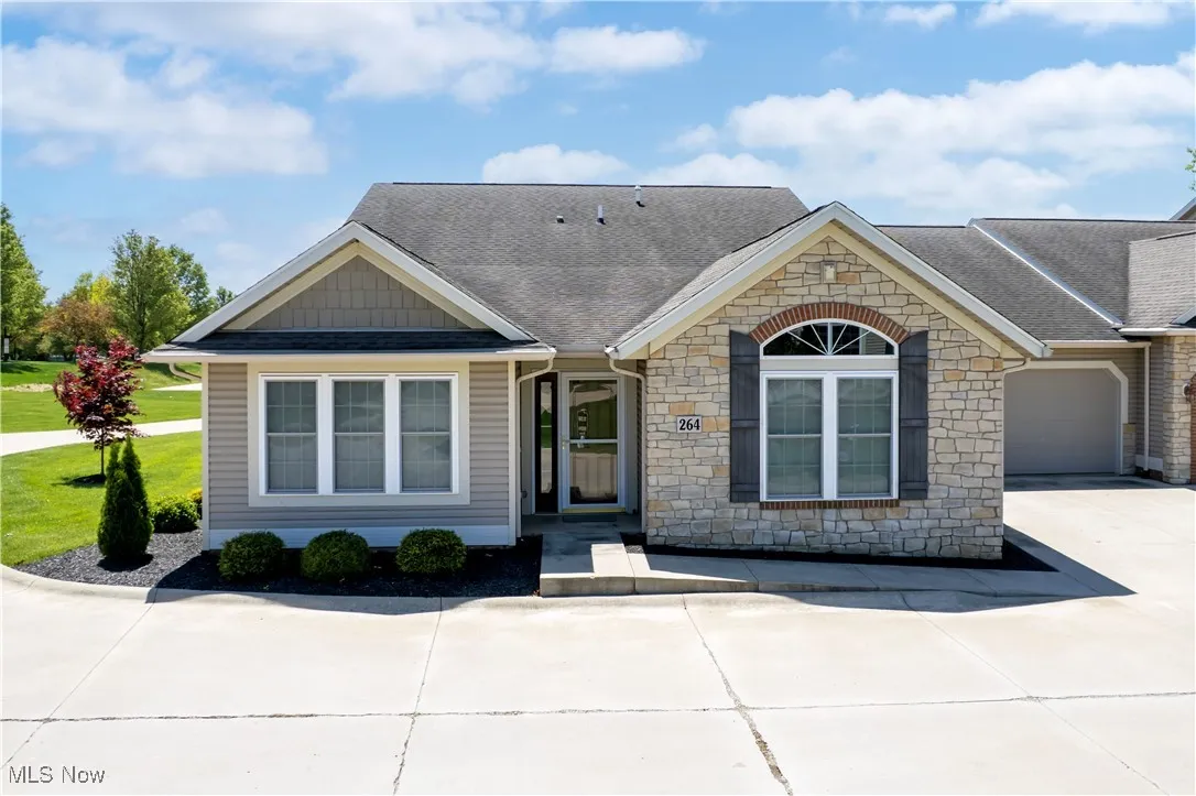 View of front facade with stone siding, a shingled roof, and driveway