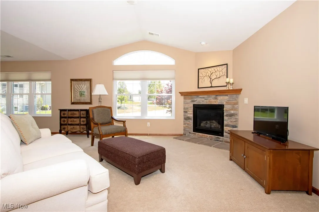 Living area featuring light carpet, vaulted ceiling, a stone fireplace, and baseboards