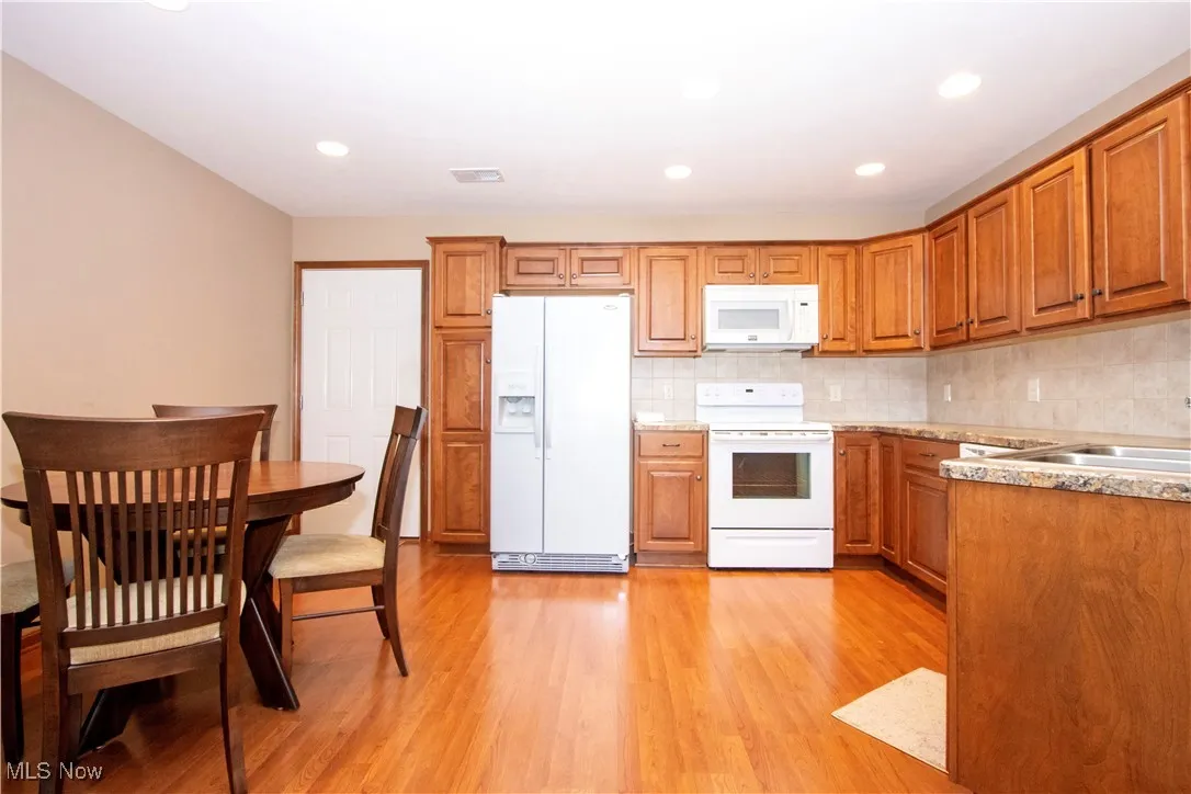 Kitchen with white appliances, brown cabinetry, light wood-type flooring, and recessed lighting