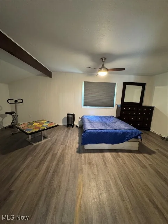 Bedroom with wood finished floors, a ceiling fan, beam ceiling, baseboards, and radiator heating unit