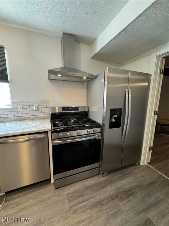 Kitchen with gas stove, range hood, dishwasher, fridge, and light wood finished floors