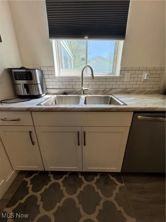 Kitchen with a sink, dishwasher, white cabinetry, light countertops, and tasteful backsplash