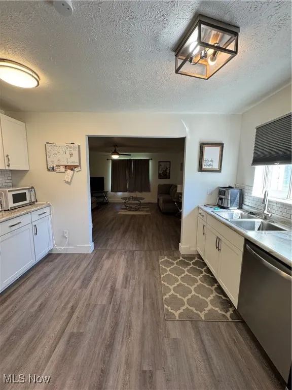 Kitchen with dishwashing machine, a sink, dark wood-type flooring, white cabinets, and a textured ceiling