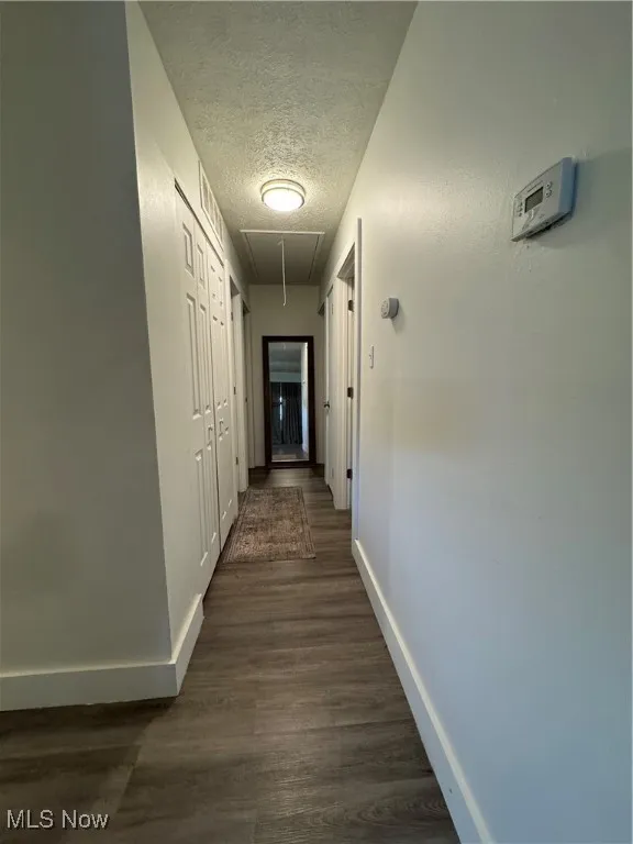 Corridor featuring attic access, baseboards, a textured ceiling, and dark wood-style floors