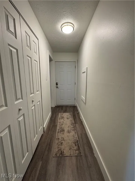 Hall with dark wood-style flooring, baseboards, and a textured ceiling