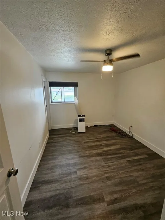Empty room with dark wood finished floors, a textured ceiling, and ceiling fan