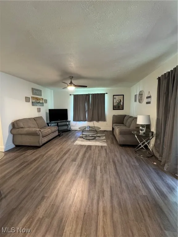 Living area featuring a textured ceiling, dark wood-style flooring, a ceiling fan, and baseboards