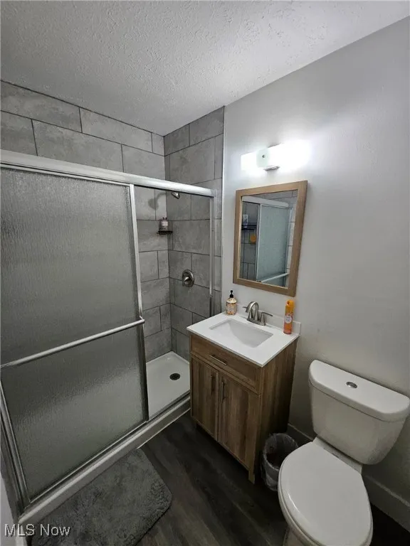 Full bath with wood finished floors, a stall shower, vanity, and a textured ceiling