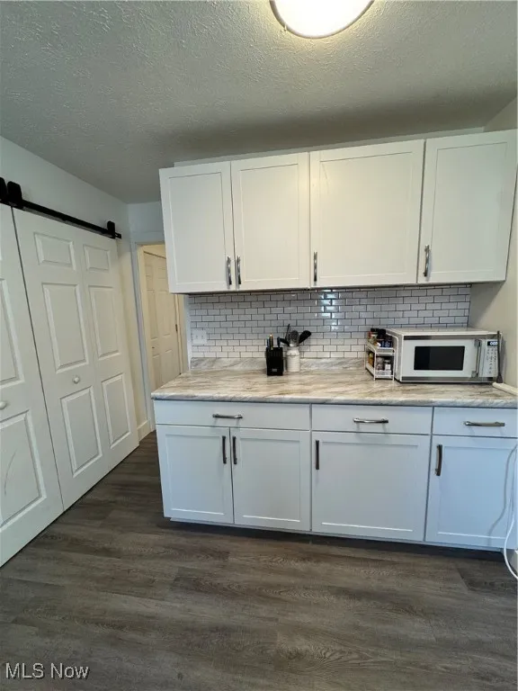 Kitchen with dark wood-style floors, white cabinetry, backsplash, a textured ceiling, and a barn door
