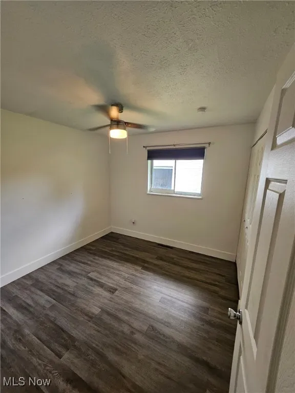 Unfurnished bedroom with dark wood-type flooring, a textured ceiling, and a ceiling fan