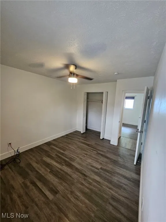 Unfurnished bedroom with a textured ceiling, dark wood-style flooring, a closet, and ceiling fan
