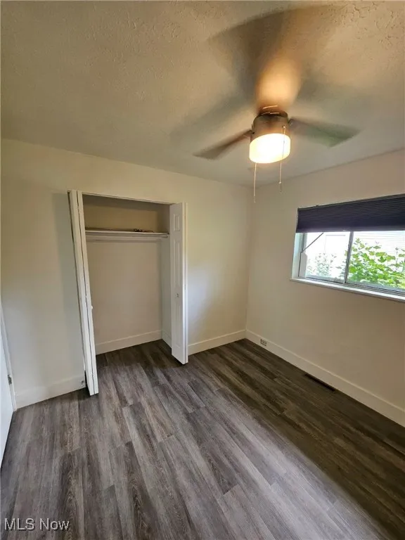 Unfurnished bedroom featuring a textured ceiling, dark wood-style flooring, a closet, and a ceiling fan