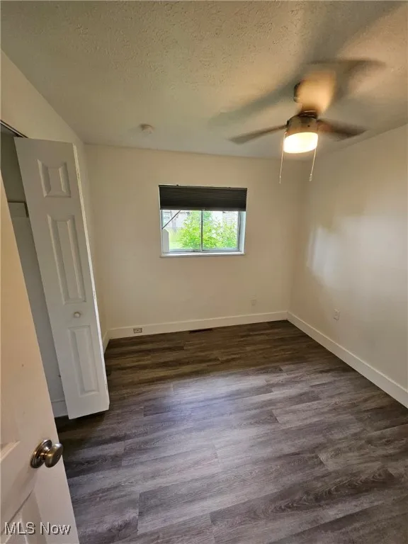 Unfurnished bedroom featuring a textured ceiling, dark wood-style floors, and ceiling fan