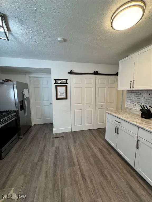 Kitchen with range, dark wood-type flooring, white cabinetry, a textured ceiling, and light countertops