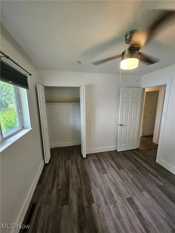 Unfurnished bedroom featuring dark wood-style floors, a closet, and ceiling fan