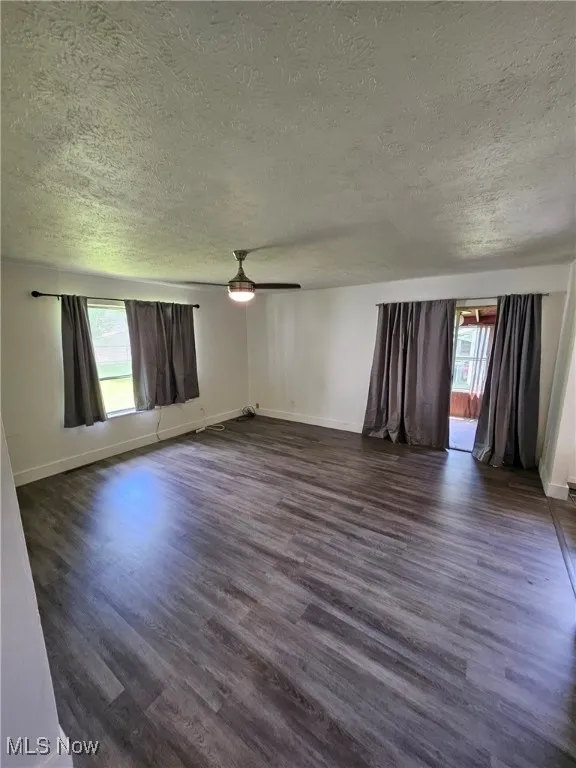 Unfurnished room with a textured ceiling, plenty of natural light, dark wood-style flooring, and ceiling fan