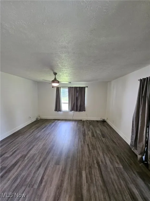 Unfurnished living room with a textured ceiling, dark wood-style flooring, and ceiling fan