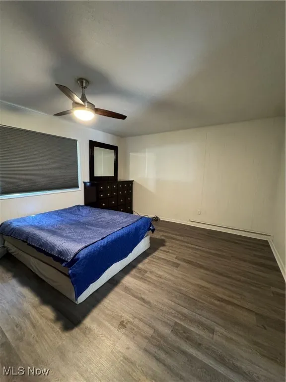 Bedroom with wood finished floors, baseboards, a baseboard radiator, and a ceiling fan