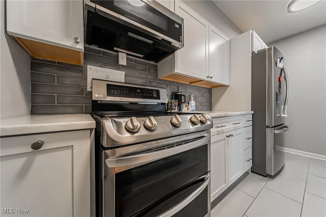 Kitchen featuring appliances with stainless steel finishes, light countertops, decorative backsplash, white cabinets, and light tile patterned floors