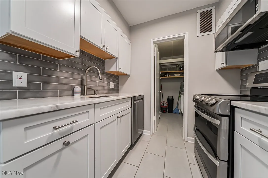 Kitchen with appliances with stainless steel finishes, backsplash, white cabinetry, and light tile patterned floors