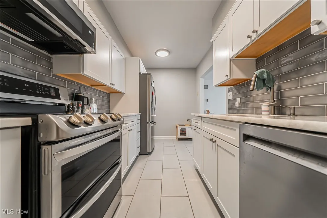Kitchen with appliances with stainless steel finishes, tasteful backsplash, and white cabinets