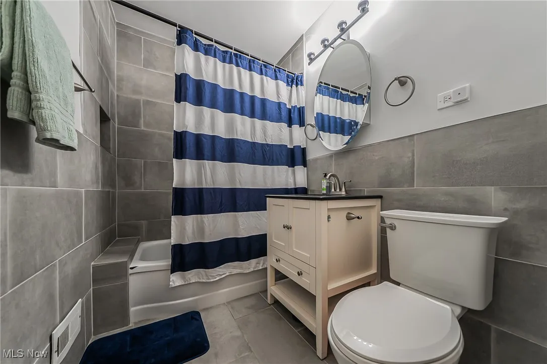 Bathroom with tile walls, tile patterned floors, shower / bath combo, and vanity