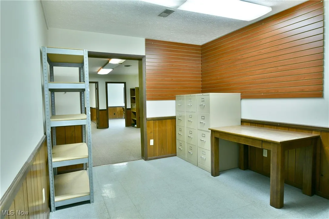 Unfurnished office featuring a wainscoted wall, wooden walls, tile patterned floors, carpet, and a textured ceiling