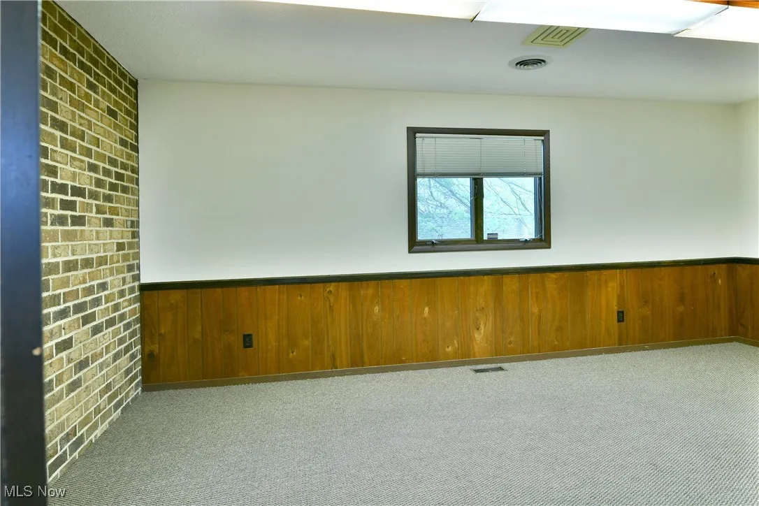 Unfurnished room featuring carpet, a wainscoted wall, and wooden walls