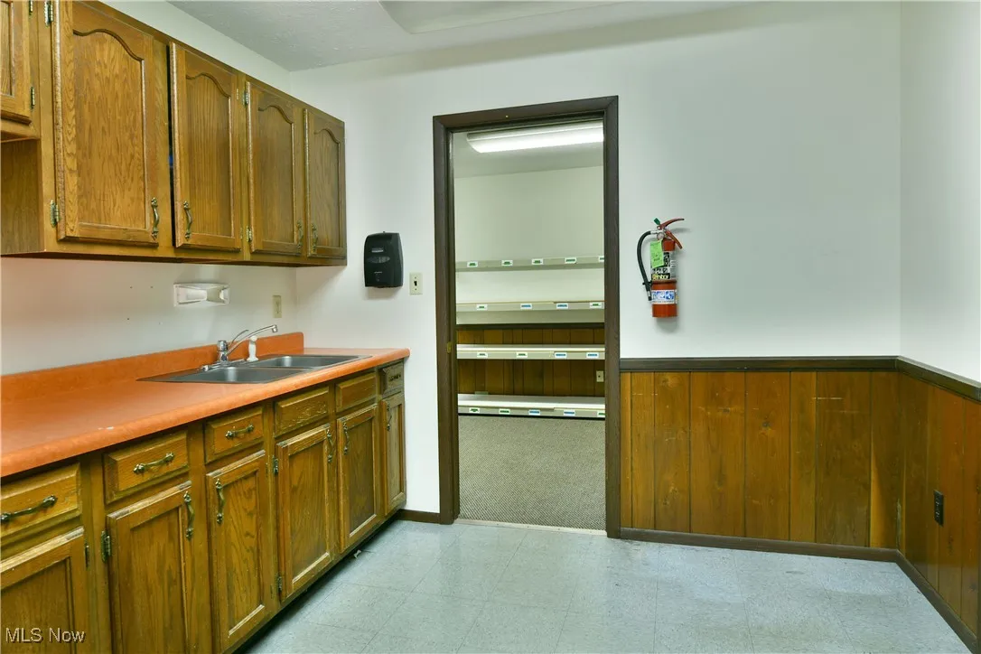 Kitchen featuring a sink, light flooring, wainscoting, brown cabinets, and wooden walls