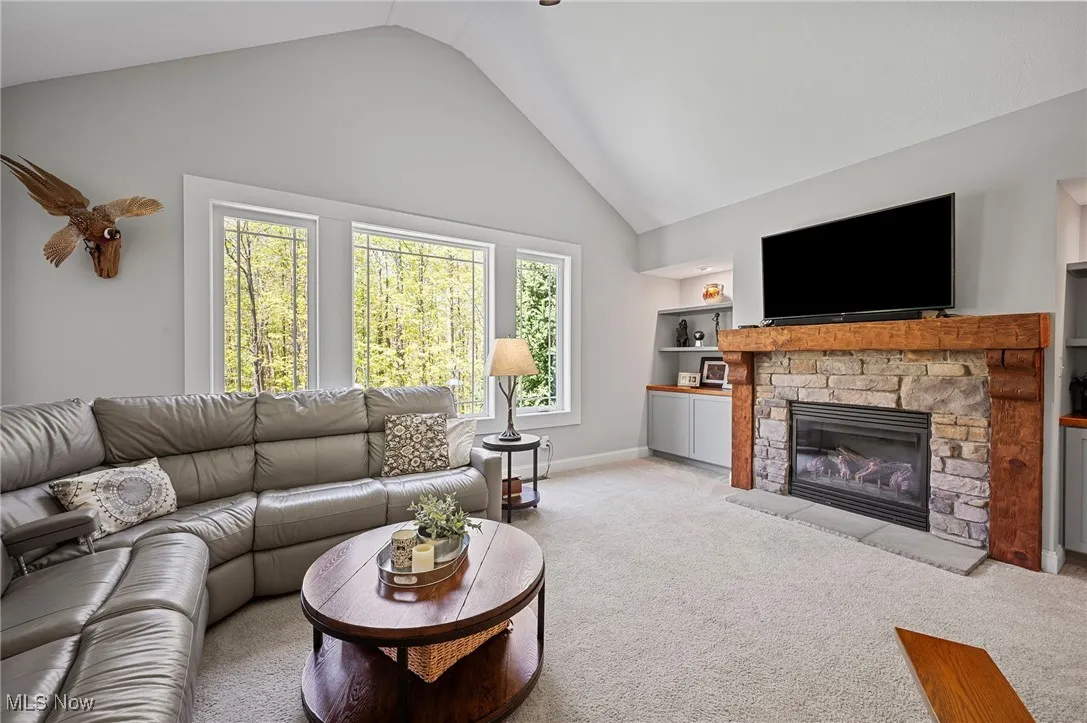 Living area with light carpet, baseboards, a fireplace, high vaulted ceiling, and built in shelves