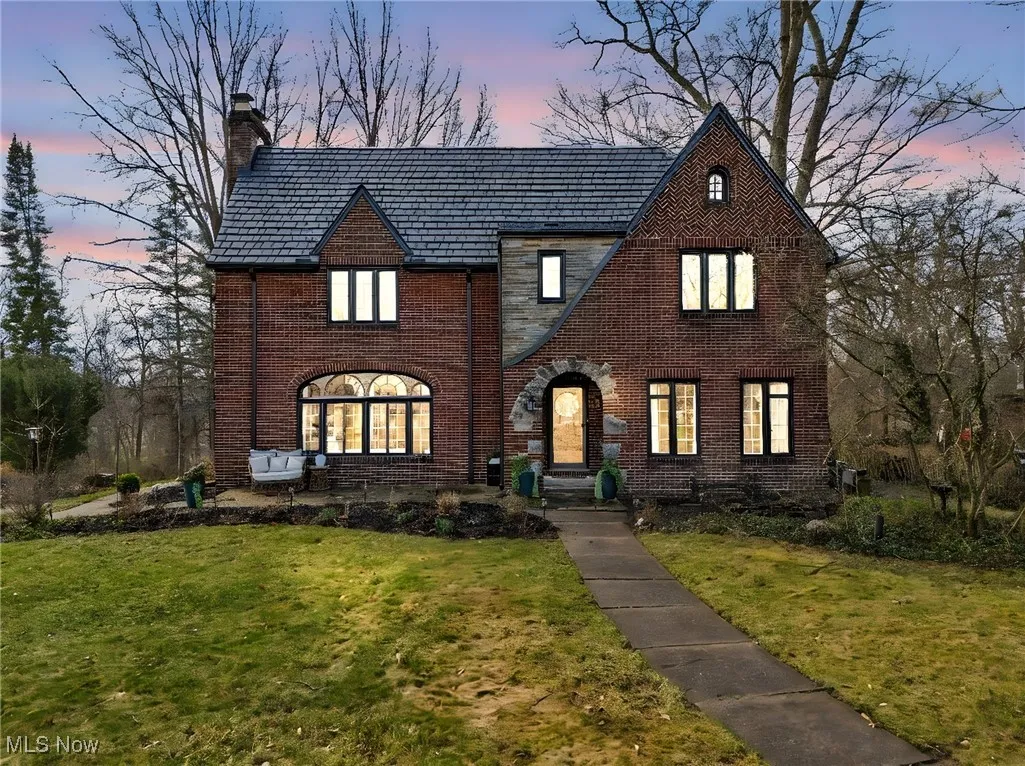Tudor home featuring a high end roof, brick siding, a chimney, and a front yard