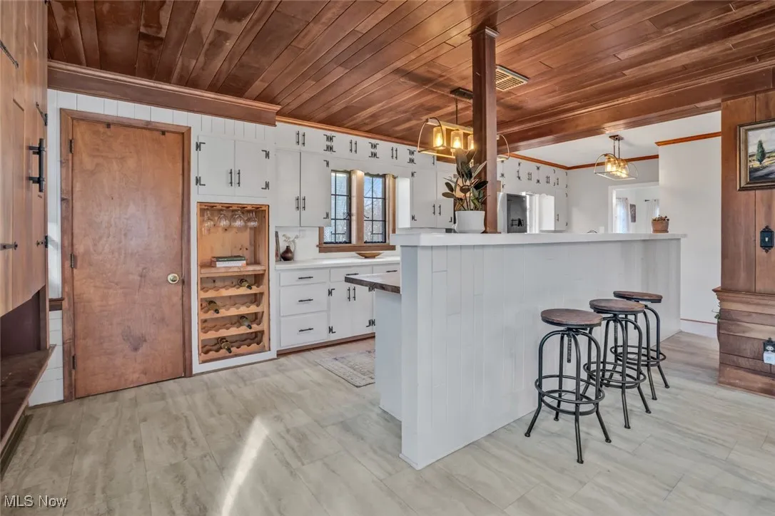 Kitchen with wood ceiling, white cabinets, a kitchen bar, ornamental molding, and decorative light fixtures