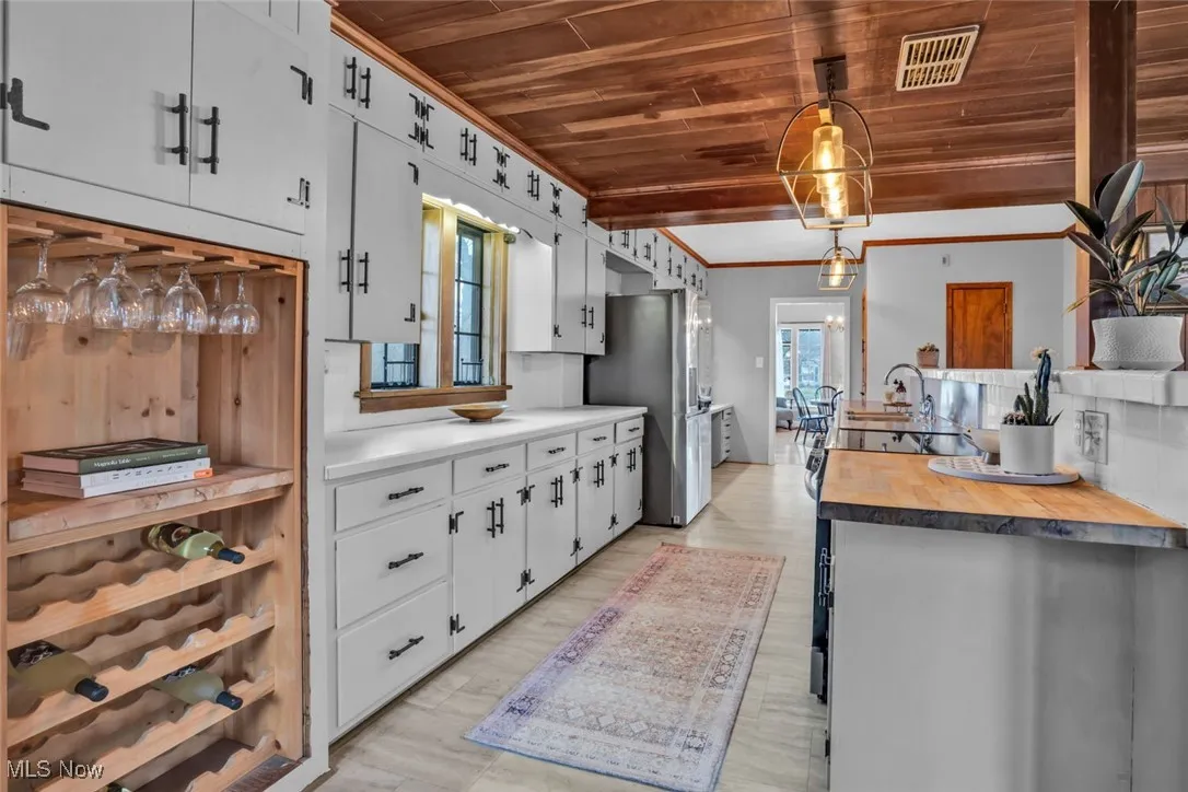Kitchen featuring wooden ceiling, freestanding refrigerator, crown molding, wood counters, and a sink