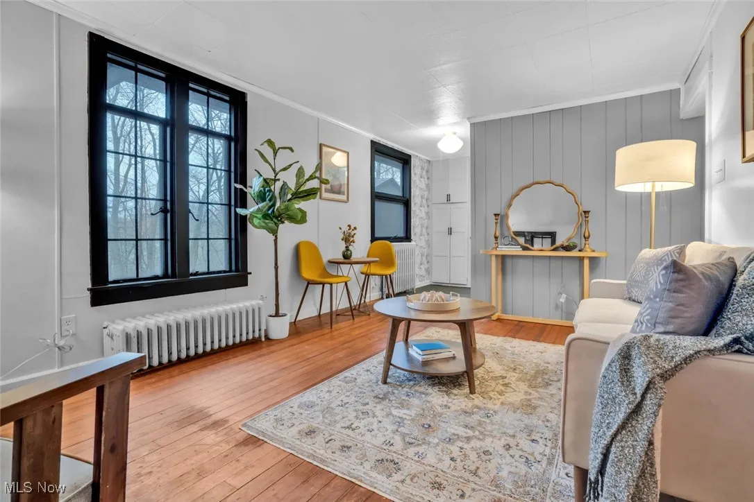 Living area with radiator, hardwood / wood-style flooring, healthy amount of natural light, and ornamental molding