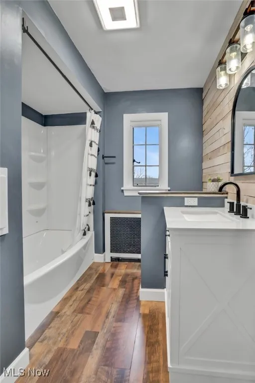Bathroom with radiator heating unit, hardwood / wood-style flooring, healthy amount of natural light, and shower / bath combo