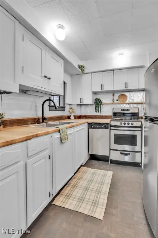Kitchen featuring appliances with stainless steel finishes, butcher block counters, white cabinets, and a sink