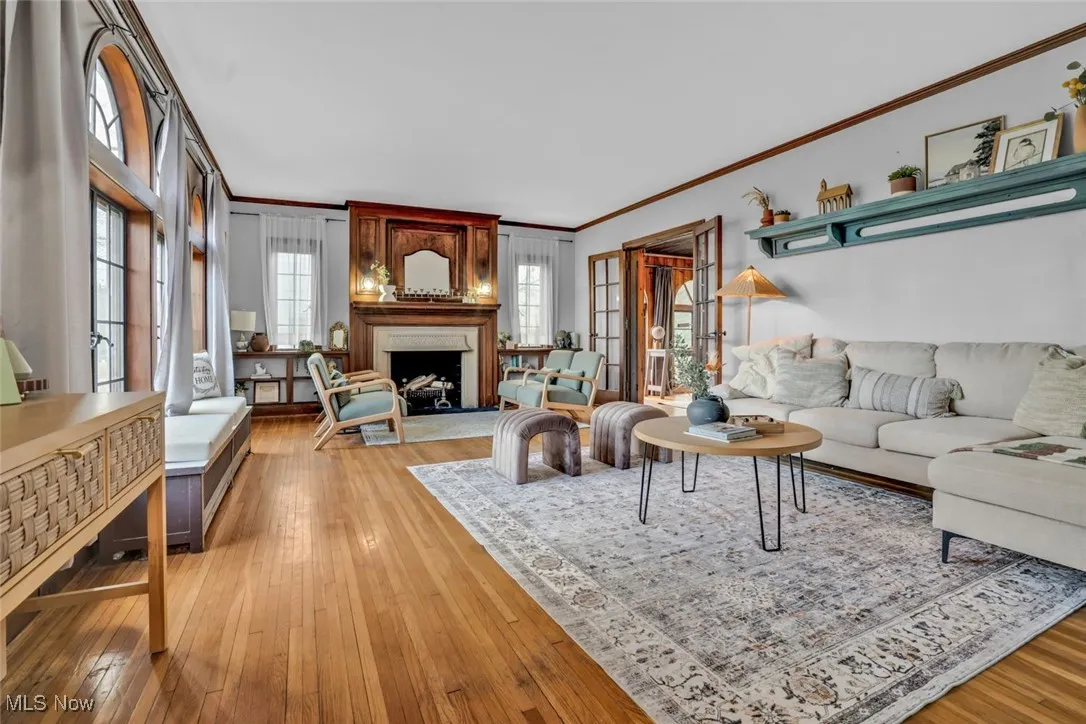 Living room with crown molding, light wood-type flooring, and a fireplace with raised hearth