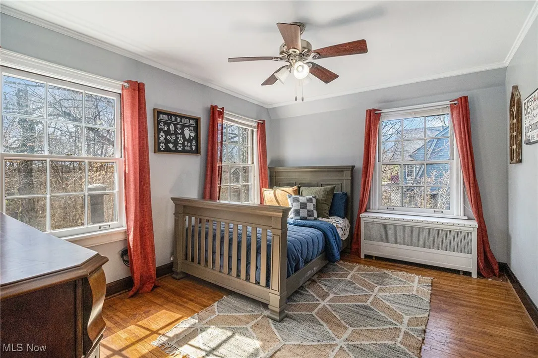 Bedroom with radiator heating unit, ornamental molding, wood finished floors, baseboards, and a ceiling fan