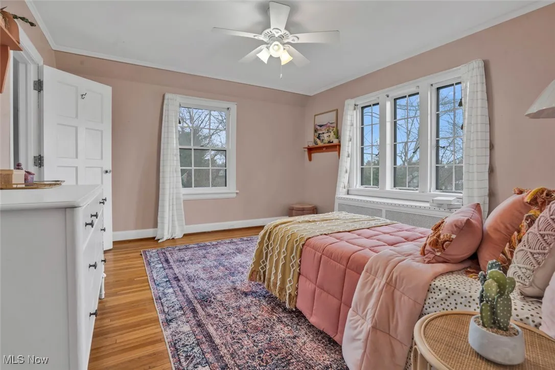 Bedroom featuring light wood-type flooring, baseboards, crown molding, radiator heating unit, and a ceiling fan