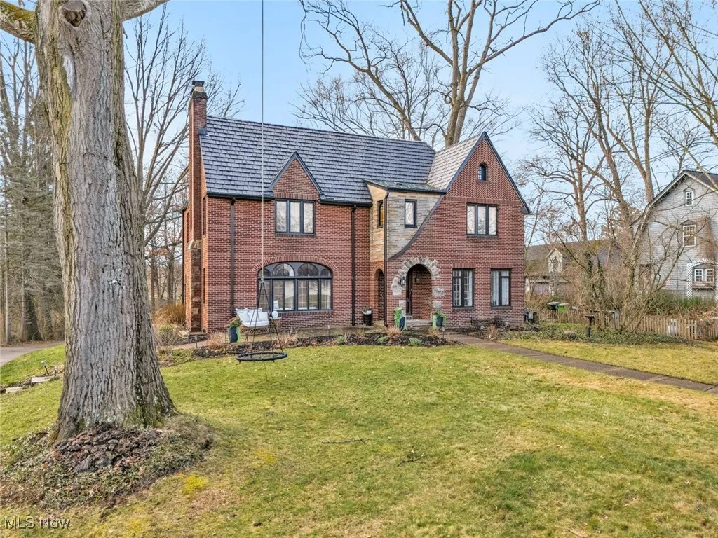 English style home with a chimney, brick siding, a front yard, and a high end roof