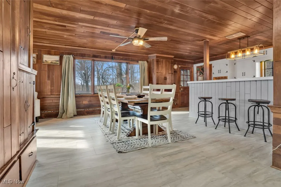 Dining space featuring wooden ceiling, wood walls, and a ceiling fan