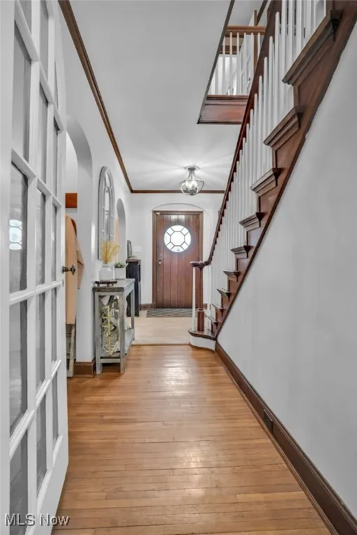 Foyer entrance with arched walkways, ornamental molding, baseboards, stairway, and wood-type flooring