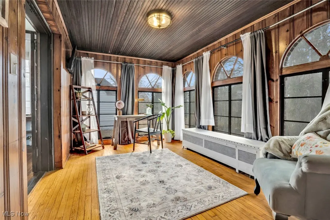 Living area with wood walls, hardwood / wood-style flooring, radiator heating unit, and wood ceiling