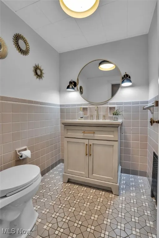 Bathroom with tile walls, wainscoting, toilet, vanity, and tile patterned floors