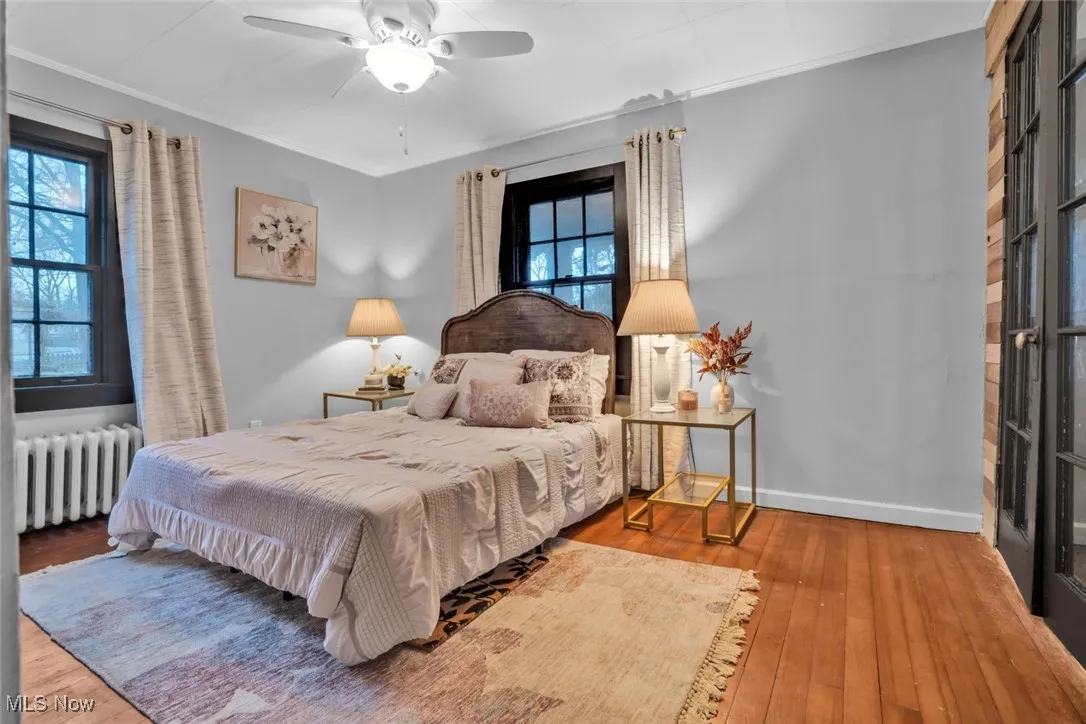 Bedroom featuring radiator, multiple windows, hardwood / wood-style flooring, crown molding, and ceiling fan