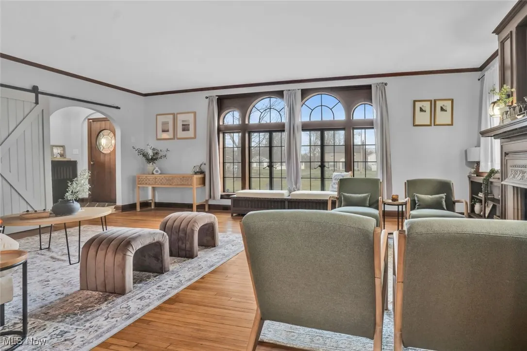 Living area featuring arched walkways, wood finished floors, ornamental molding, baseboards, and a barn door