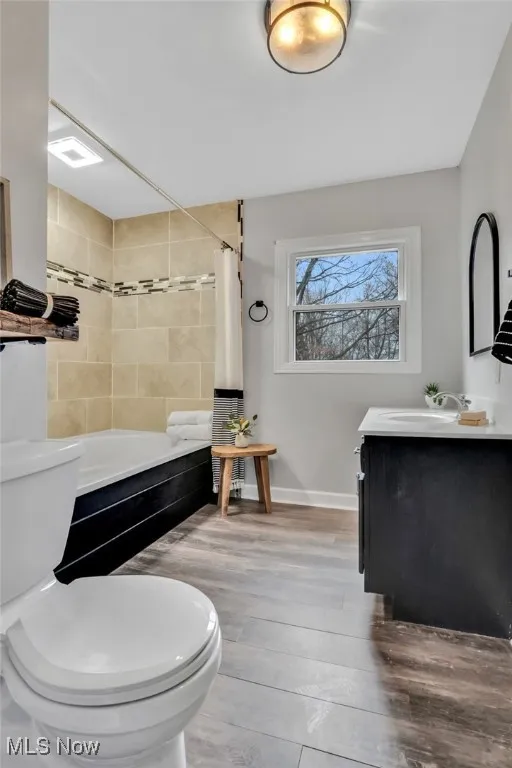 Full bath featuring toilet, shower / bath combo, wood finished floors, baseboards, and vanity
