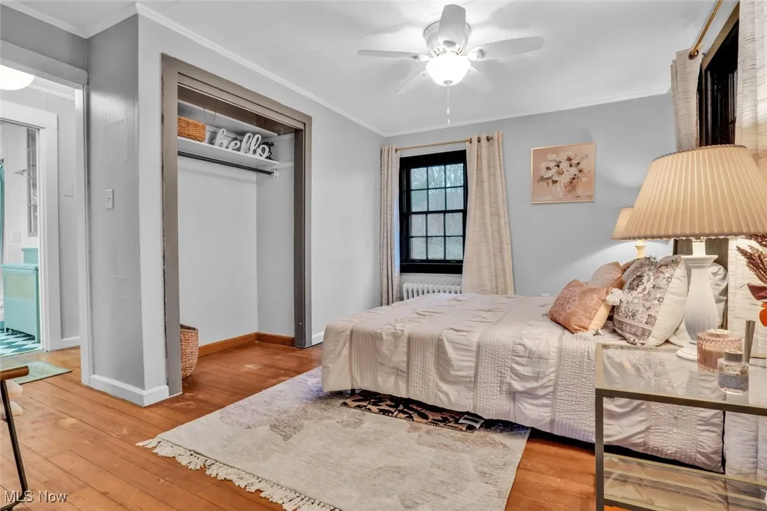 Bedroom featuring hardwood / wood-style floors, a closet, crown molding, radiator heating unit, and baseboards