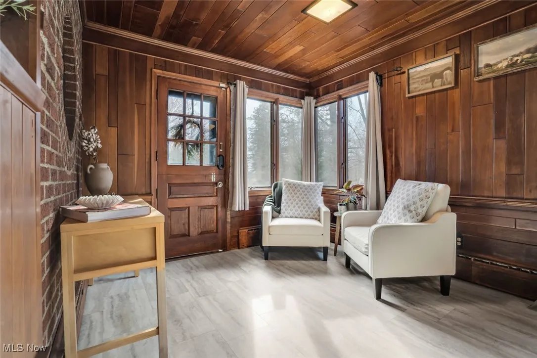 Sitting room featuring wooden walls, wooden ceiling, plenty of natural light, and ornamental molding